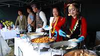 Fünf Personen in traditioneller nepalesischer Kleidung teilen Essen aus.