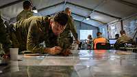Ein Soldat lehnt über einem Tisch mit einer Karte und macht auf ihr Notizen.