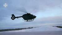 Ein Hubschrauber vom Typ H145M fliegt dich über ein verschneites Gelände