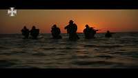 Silhouetten von bewaffneten Soldaten, die zu Fuß aus dem Wasser kommen bei Dämmerung
