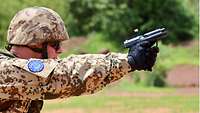 Ein Soldat mit Helm und Schießbrille gibt mit der Pistole einen Schuss ab, die Hülse fliegt aus dem Verschlussfenster