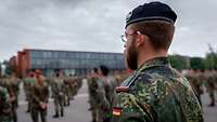 Aufnahme über die Schulter eines Soldaten. Zahlreiche Offizieranwärter sind auf einem großen Platz angetreten.