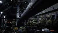 Soldaten stehen im Laderaum eines A400M neben einem Hubschrauber vom Typ H145M bei Dunkelheit