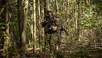 Zwei Soldaten bewegen sich hintereinander im Gefechtsanzug mit Tarnschiminke im Gesicht durch einen Wald.