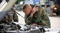 Ein Soldat hat die Motorhaube eines Fahrzeuges geöffnet und prüft es auf mögliche Beschädigungen