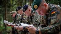 Vier Soldaten sitzen nebeneinander im Wald und lesen Schriftstücke.