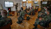 Soldaten sitzen in einem Raum. Vorn steht ein Soldat an einem Whiteboard und spricht.