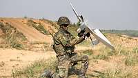 Ein Soldat kniet und nimmt eine gelandete Drohne auf