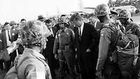 Schwarz-Weiß-Bild: US-Präsident John F. Kennedy steht zwischen amerikanischen Soldaten