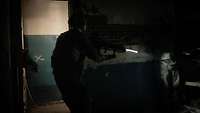 Ein Soldat betritt einen sehr dunklen Raum. In einer Ecke steht ein bewaffneter Mann der einen feindlichen Akteur simuliert.