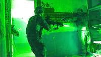 Durch ein Nachtsichtgerät sind zwei Soldaten erkennbar. Das Bild ist grün.