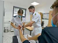 Eine Soldatin und ein Soldat in weißer Arztkleidung begutachten den Fuß eines Patienten, der auf einer Liege sitzt.