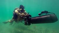 Ein Kampfschwimmer mit Unterwasserscootern unter Wasser