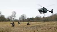Vier Soldaten seilen sich aus einem Hubschrauber ab und nehmen Stellung auf einer Wiese ein