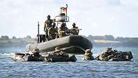 Bewaffnete Kampfschwimmer in Stellung im Wasser, ein Schlauchboot mit Soldaten dahinter
