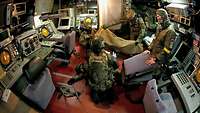 Soldaten in der Operationszentrale unter Deck eines Schiffes hocken und stehen um einen am Boden liegenden Verwundeten