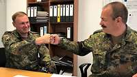 Zwei Soldaten in Uniform sitzen an einem Schreibtisch im Büro und legen ihre Fäuste aneinander.