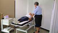 Frau liegt auf Liege und Ihr Blutdruck wird von einem Arzt gemessen.