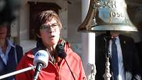 Eine Frau in roter Jacke spricht in unterschiedliche Mikrofone.