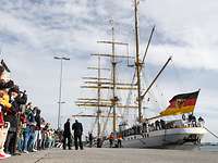 Mehrere Menschen blicken auf ein weißes Segelschulschiff der Deutschen Marine.