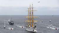 Ein weißes Segelschulschiff der Deutschen Marine in Begleitung von mehreren kleineren Booten in See.