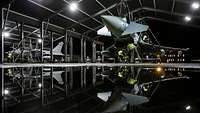 Ein Eurofighter wird in einer Halle von Technikern kontrolliert.