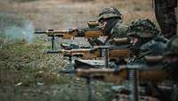 Soldiers are lying side by side, firing their rifles.