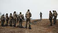 Soldiers are standing around a terrain sand table; the officer in charge is standing in front of them.