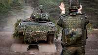 Guided by a soldier, a tank crosses a military bridge. 