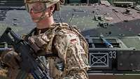 An armed soldier is standing in front of a tank with a military symbol and the number 33.