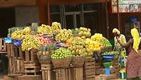 Zwei Frauen stehen an einem Stand voller Bananen, Ananas und anderem Obst