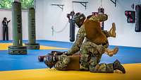 Ein Soldat liegt auf dem gelb-blauen Hallenboden, ein zweiter hockt über ihm. Sie kämpfen.