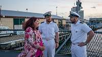 Eine Frau in einem geblümten Kleid im Gespräch mit Marineoffizieren in weißer Uniform.