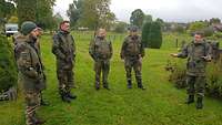 Eine Gruppe von Soldaten in Uniform steht im Halbkreis auf einem Friedhof