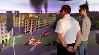 zwei Männer stehen vor einer Projektionsfläche mit einem brennenden Gebäude