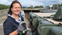 A woman stands in front of a loaded railroad car and holds a screw hook in her hand.