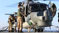 Mehrere Soldaten stehen um einen Hubschrauber, zwei von ihnen betanken den Sea Lynx