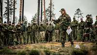 Eine norwegische Soldatin steht in einem Geländesandkasten und hat einen Stock in der Hand. Im Hintergrund viele Soldaten. 
