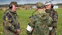 Drei Soldaten in Uniform stehen auf einer Wiese auf dem Übungsplatz zusammen.