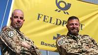 Zwei Soldaten stehen vor der Flagge der Feldpost