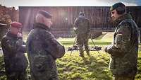 Drei Soldaten stehen beisammen und sprechen miteinander, im Hintergrund eine Schießausbildung.