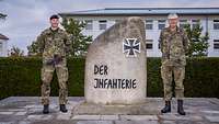 Zwei Soldaten stehen links und rechts neben einem Stein, auf dem „Der Infanterie“ steht.