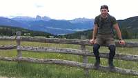 Ein Soldat sitzt in Sportklamotten auf einem Zaun. Im Hintergrund die Dolomiten 