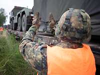 Soldat mit Helm und Warnweste steht neben Waggon und weist Lkw per Handzeichen ein