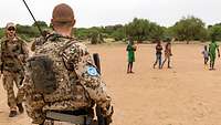 Drei Soldaten und mehrere Kinder, die einen orangen Fußball haben