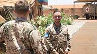 Ein Soldat unterhält sich mit einem anderen Soldaten. Im Hintergrund ein Sanitäts-Lkw mit rotem Kreuz sowie Zelte