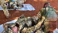 Ein verletzter Soldat liegt am Boden und verzieht schmerzerfüllt sein Gesicht. Ein weiterer Soldat versorgt die Wunden.