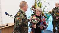 Ein Soldat fasst eine Zivilistin an die Schulter. Sie hält einen Blumenstrauß in der Hand und schaut ihn an.