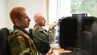 Soldaten sitzen vor Computern in einem Raum und hören einem Dozenten zu.