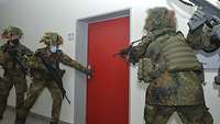 Links und rechts von einer roten Tür stehen je zwei bewaffnete Soldaten. Einer hält die Hand an der Türklinke.